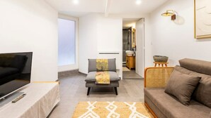 A modern living room with a flat-screen TV, a grey sofa, a patterned rug, and a wicker side table. - Bellecour Pavillon (Lyon)