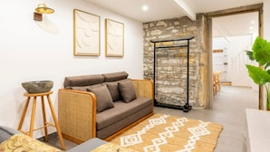 A modern living room with a sofa, a small side table, a patterned rug, and a stone wall. - Bellecour Pavillon (Lyon)