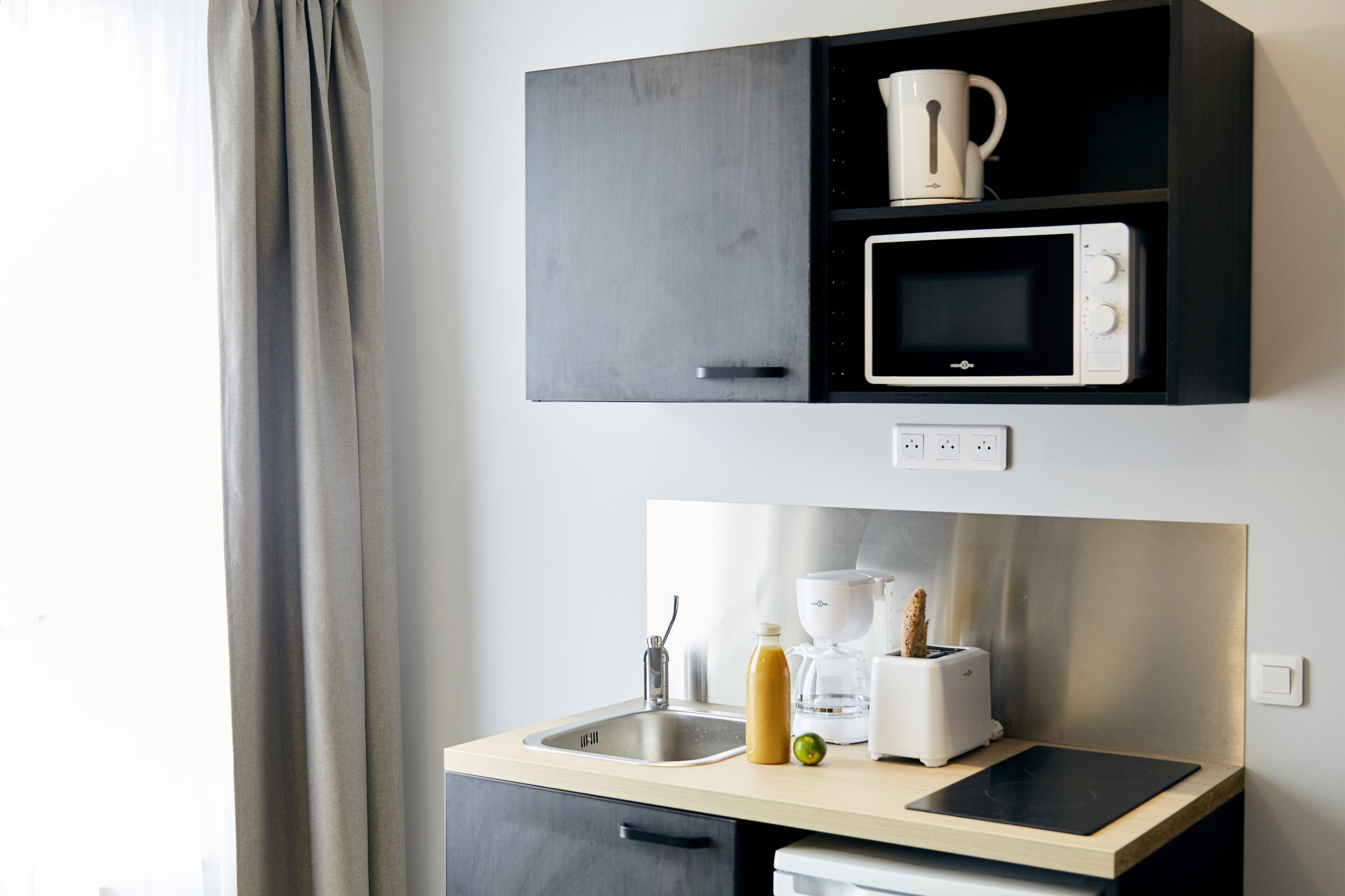 A modern kitchen with a microwave, toaster, and coffee maker on the countertop, and a cabinet above with a mug.