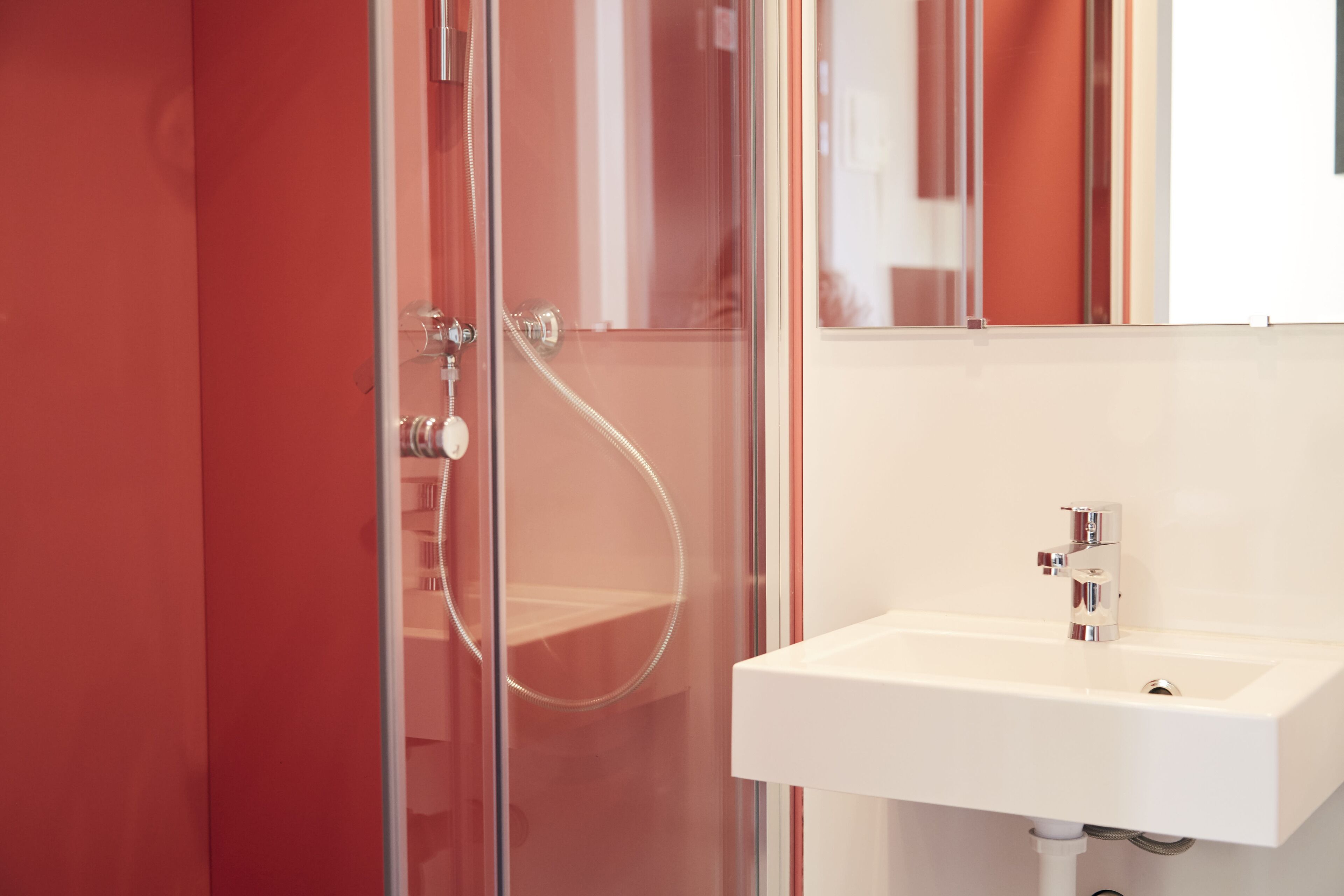 Un bany modern amb una cabina de dutxa de vidre, un lavabo blanc i un mirall sobre el lavabo.