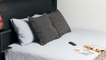 A neatly made bed with a grey sheet, a black pillow with a geometric pattern, and a remote control on the bed.