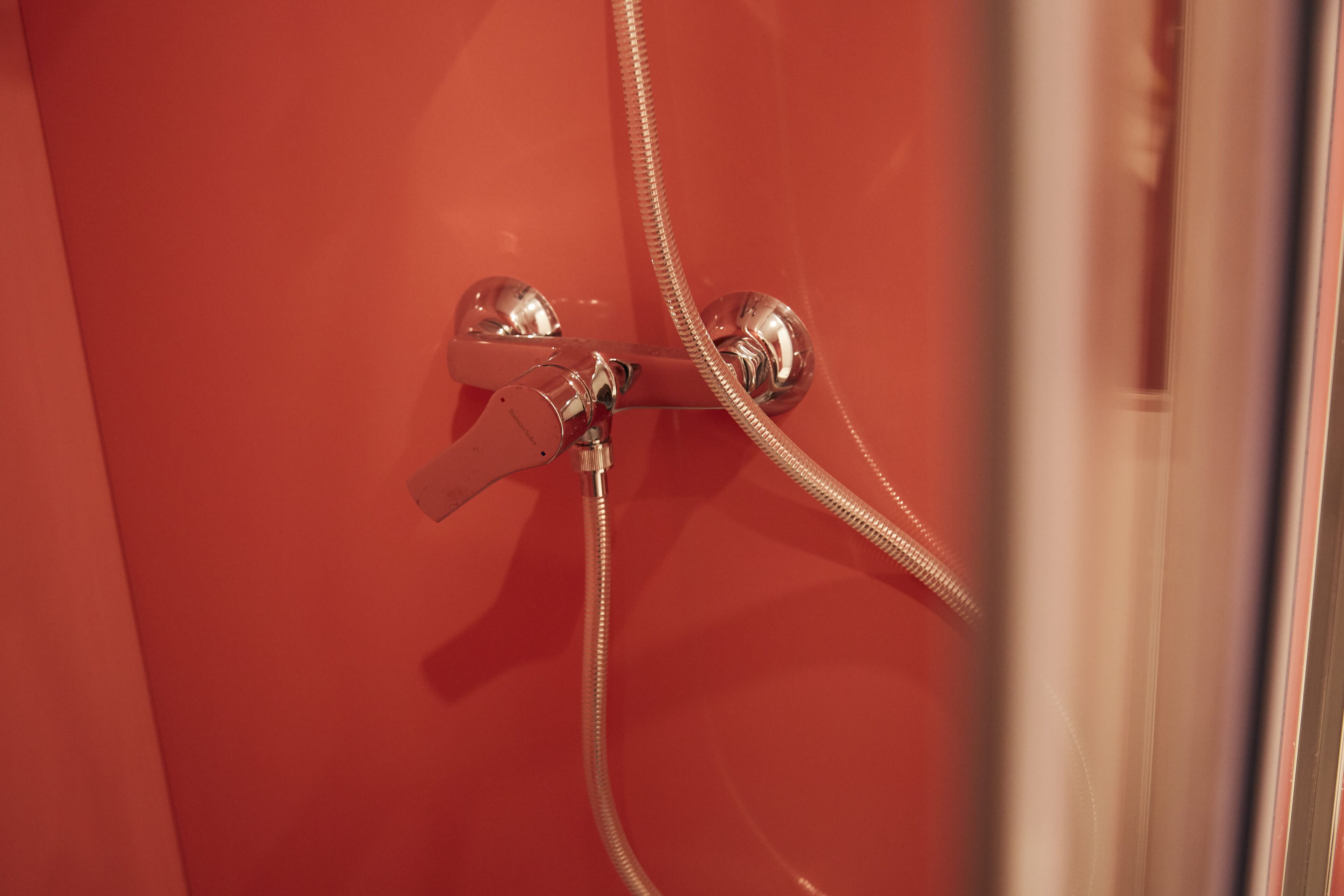 A bathroom with a red wall, a shower with a chrome faucet, and a visible shower hose.