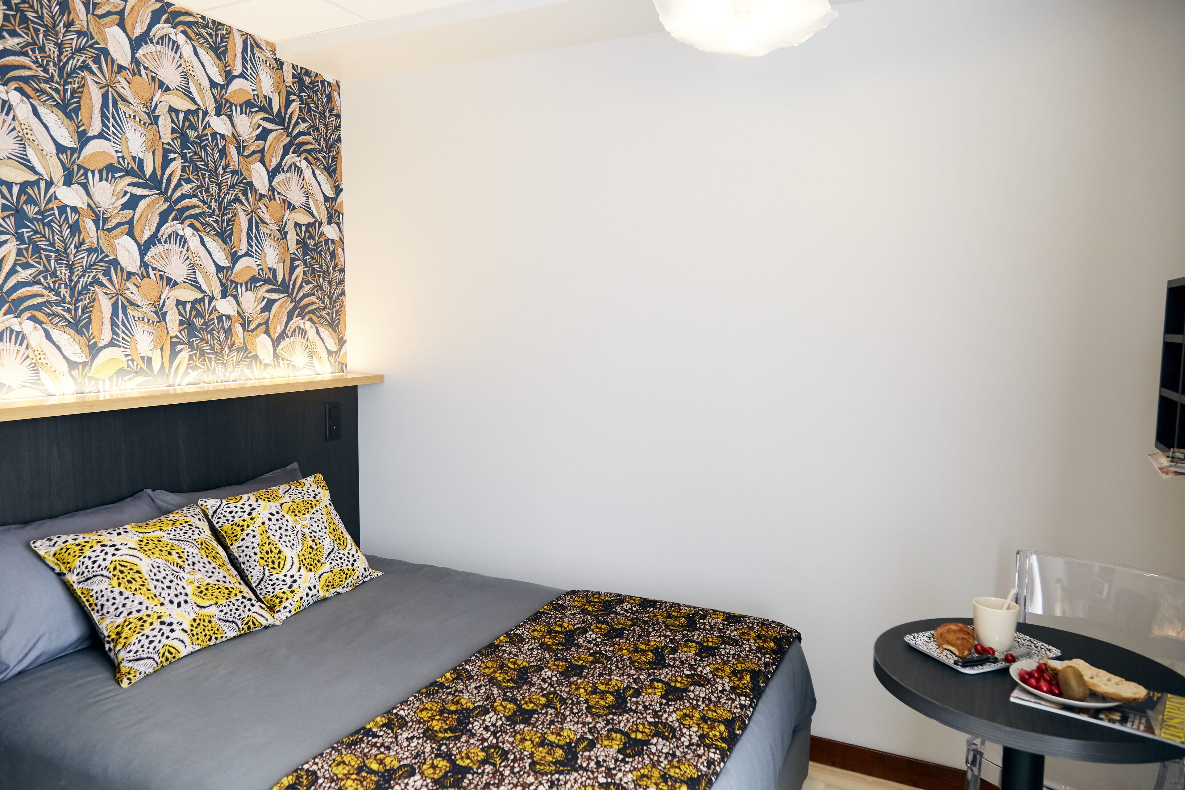 A hotel room with a bed, a table with breakfast, and a wall with a floral pattern.