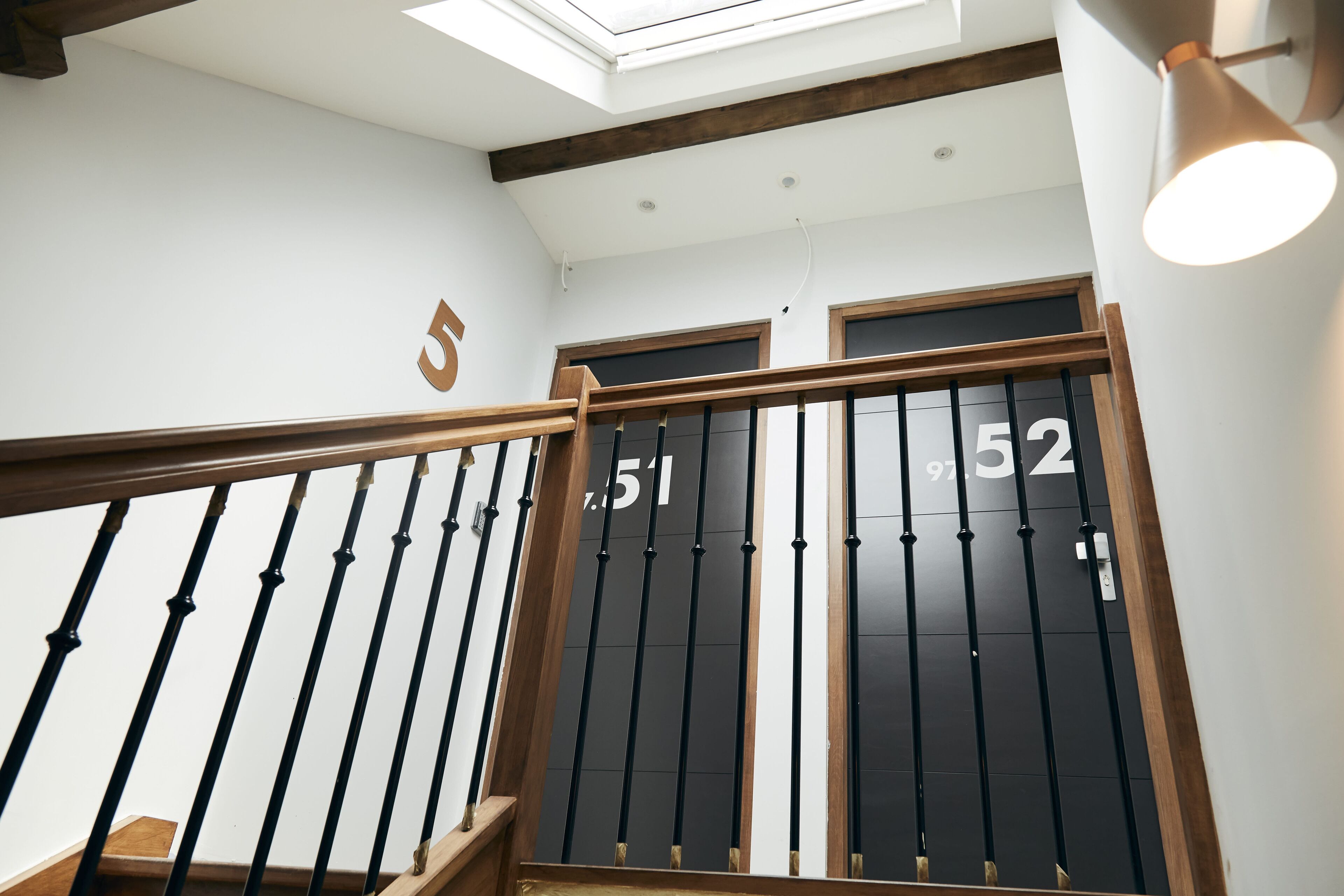 A staircase with black railings and wooden steps, leading to a door with the number 52.