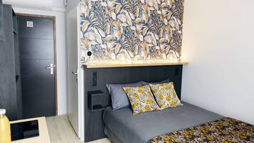 Ein kleines Schlafzimmer mit einem Bett, einer an der Wand befestigten Ablage, einer Tür mit einem 'Betreten verboten'-Schild und einem gemusterten Kopfteil.