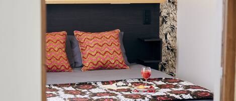 Una cama bien hecha con almohadillas estampadas, una mesita de noche y una bandeja con bebidas y aperitivos.