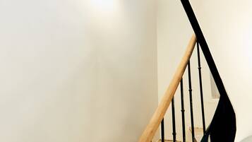 A modern staircase with a wooden handrail and black balusters, leading to a landing with a white wall and a light fixture.