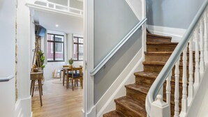 Eine Treppe mit Holzbodenstufen und weißen Geländern, die zu einem Raum mit Holzdielen und einem Essbereich mit Tisch und Stühlen führt.