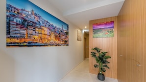 A hallway with a large cityscape painting, a smaller landscape painting, and a potted plant. - GuestReady - Olivieri's House - 1 (Porto)