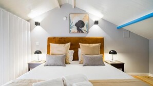 A bedroom with a large bed, two bedside tables with lamps, a wooden headboard, and a wall-mounted artwork.