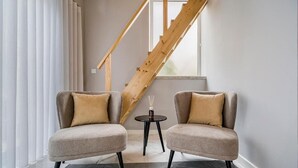 A room with two armchairs, a small table, and a wooden staircase.