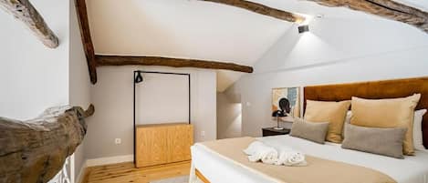 A bedroom with a wooden ceiling, a bed with beige bedding, a nightstand, and a mirror.
