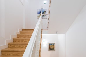 Un escalier avec des marches en bois et des rampes blanches, menant à un palier où est accrochée une image encadrée.