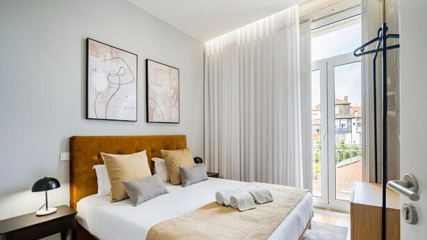 Quarto de hotel moderno com uma cama, mesa de cabeceira, escrivaninha e vista para a cidade pela janela.