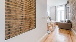 Uma sala de estar moderna com piso de madeira, um sofá cinza e um espaço de jantar com mesa e cadeiras brancas.