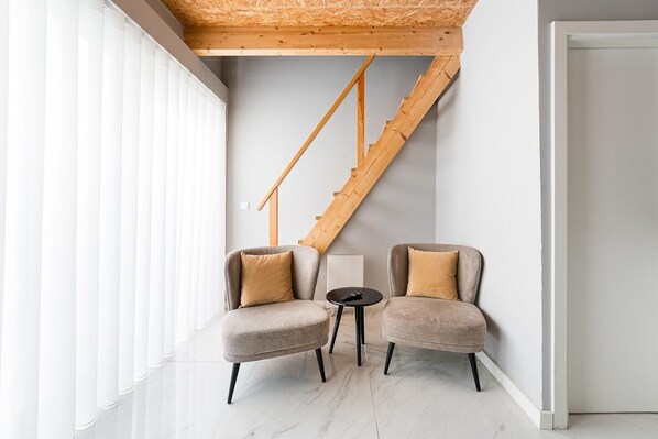 A modern interior with a wooden staircase, two armchairs, a small round table, and a white radiator.