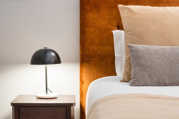 A neatly made bed with a headboard, a bedside lamp, and a small nightstand.