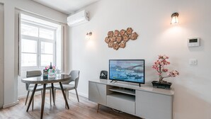 Een moderne woonkamer met een televisie, een eettafel, stoelen en een decoratief kunstwerk.