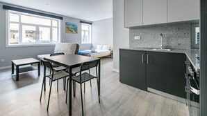 A modern kitchen with dark cabinets and a granite countertop, a dining area with a wooden table and chairs, and a bedroom with a bed and window. - GuestReady - Olivieri's House - 3 (Porto)