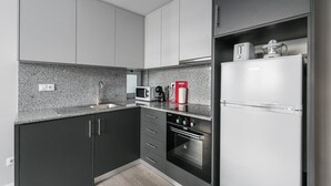 A modern kitchen with dark cabinets, a granite countertop, a built-in oven, a microwave, a coffee machine, and a refrigerator. - GuestReady - Olivieri's House - 3 (Porto)