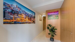 A hallway with a large cityscape painting, a smaller landscape painting, and a potted plant. - GuestReady - Olivieri's House - 3 (Porto)