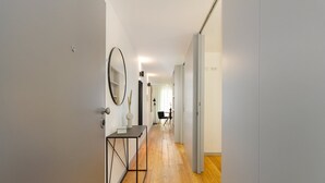 Un pasillo con suelo de madera, una consola con espejo y una silla al fondo.