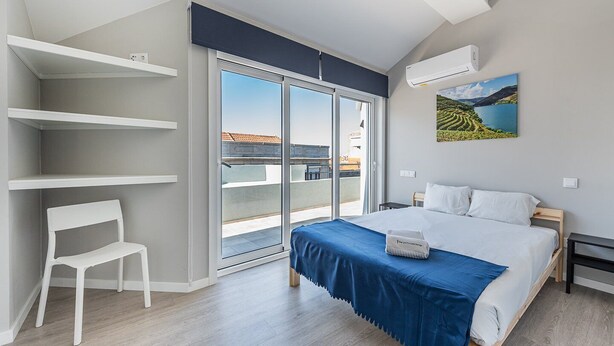 A modern bedroom with a large bed, a chair, a balcony with a view, and a painting on the wall.