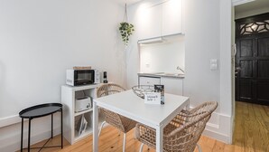 Eine kleine Küche mit weißen Schränken, einer Mikrowelle, einem Toaster und einem Korbstuhl.