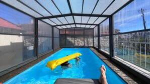 En pool med en glasvägg runt om, en gul uppblåsbar badleksak och en person som kopplar av i en solstol.