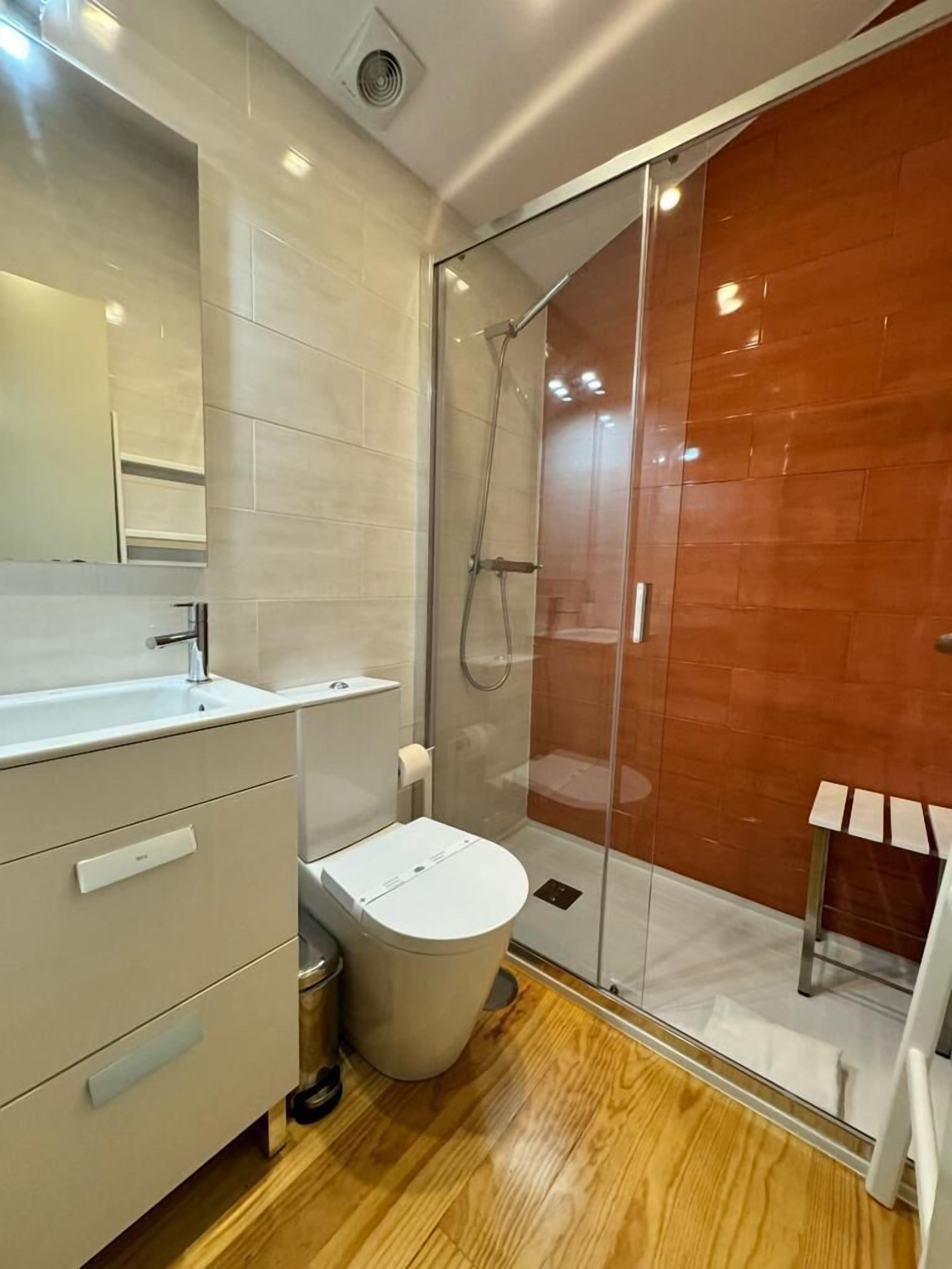 A modern bathroom with a glass-enclosed shower, a toilet, and a vanity with drawers.