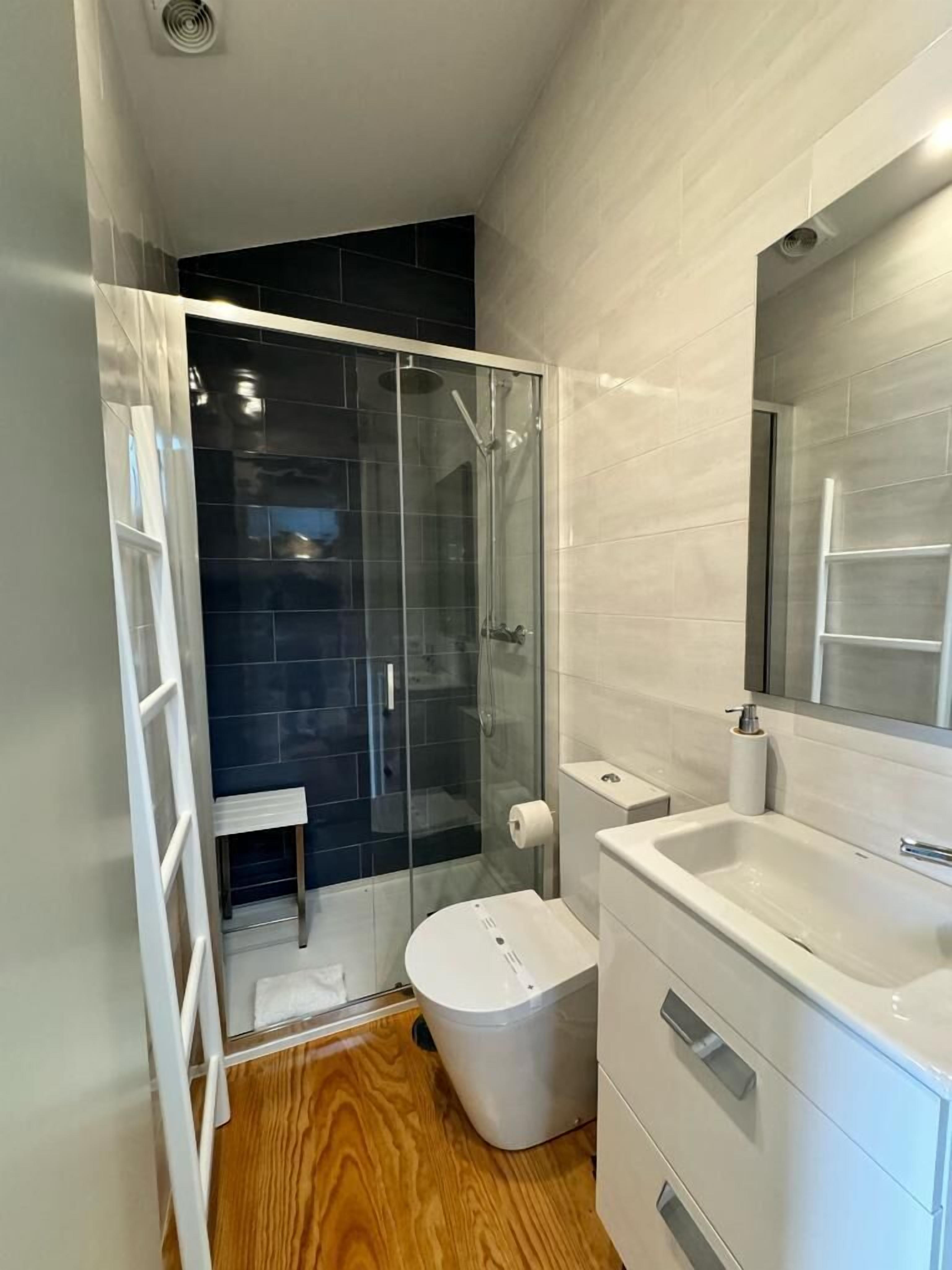 Une salle de bain moderne avec une douche à parois de verre, des toilettes blanches et un lavabo avec un miroir.