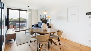 A modern living room with a round dining table, comfortable seating, and a large window offering a view of the outdoors. - GuestReady - Asaf's Magnolias Retreat (Vila Nova de Gaia)