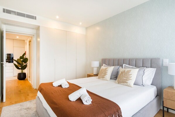 Ein modernes Hotelzimmer mit einem großen Bett, einem grauen gepolsterten Kopfteil und einem hölzernen Nachttisch.