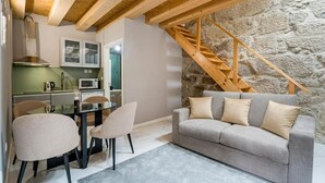 Una sala de estar acogedora con pared de piedra, una escalera de madera, un sofá gris y una mesa de comedor con sillas.