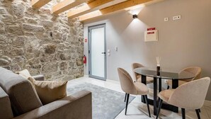 Una habitación acogedora con pared de piedra, techo de madera, puerta de cristal, una mesa redonda con sillas y un sofá.