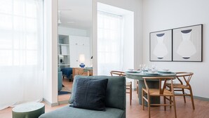 Moderni olohuone, jossa on sohva, ruokapöytä tuoleineen ja taustalla keittiötila.
