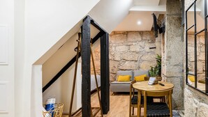 A cozy room with a stone wall, a wooden table, and a sofa with yellow cushions. - GuestReady - Caldeireiros Building (Porto)