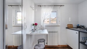 A compact kitchen with a dining area, a window with curtains, a radiator, and a striped rug. - Garden-inspired retreat (Celeiros)