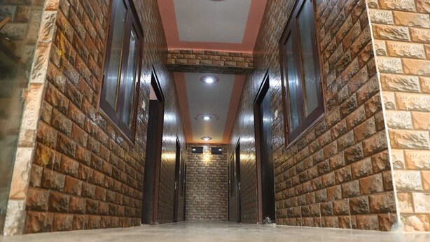 A hallway with brick walls and a tiled floor, leading to a room with a visible door. - Shri Laddu Gopal Guest House (Mathura)