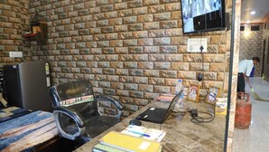 A room with a stone wall, a desk with a laptop, a chair, a bed, and a television displaying security footage. - Shri Laddu Gopal Guest House (Mathura)