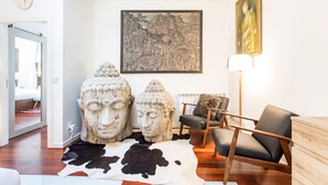Ein modernes Wohnzimmer mit Kuhfellteppich, einer Holzkommode, einem schwarzen Ledersessel und einem großen gerahmten Gemälde an der Wand.
