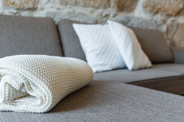 A grey sofa with a rolled white blanket and two white pillows.