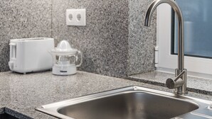 Una cocina con un lavamanos de acero inoxidable, un tostador y un exprimidor sobre una encimera de granito.