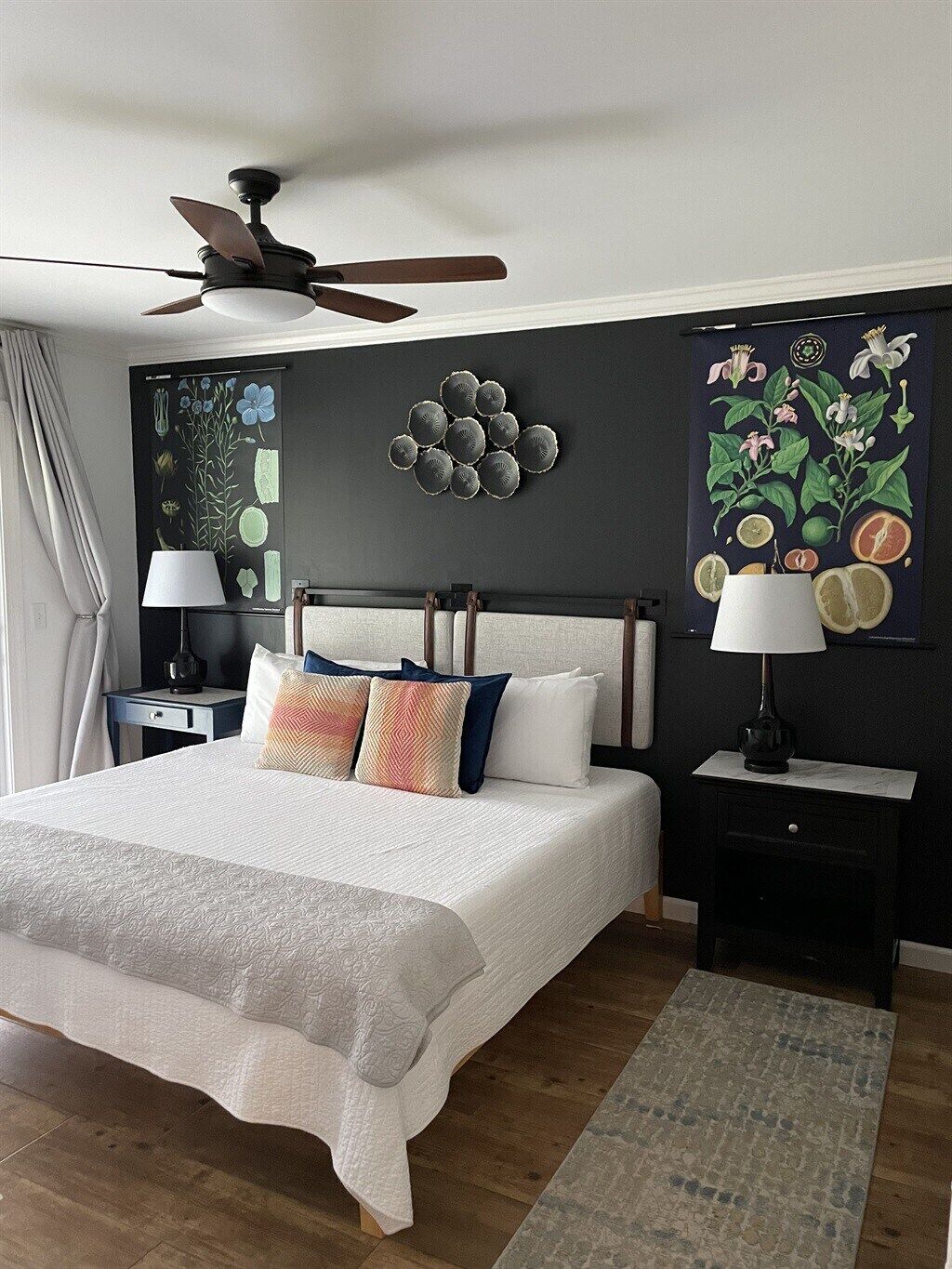 A bedroom with a bed, nightstands, a ceiling fan, and wall art.