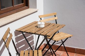 Una pequeña mesa de madera con un objeto blanco encima, ubicada frente a una pared con una ventana arriba.