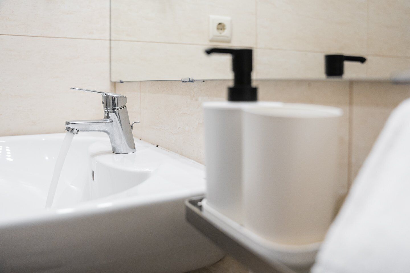 A bathroom sink with running water, a soap dispenser, and a toilet paper holder.