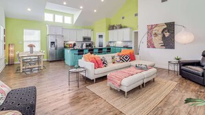 A spacious living area with a dining table, a sofa, and a kitchen in the background. - Brito Beach- View of Pond | Propane Grill (Port Aransas)