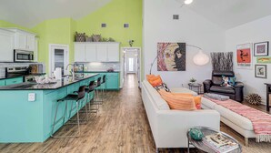 A modern kitchen with a teal island, white cabinets, and a dining area with bar stools. - Brito Beach- View of Pond | Propane Grill (Port Aransas)