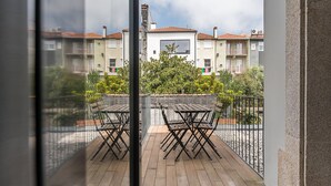 Un balcón con dos mesas y sillas de madera, baranda metálica y vista de edificios residenciales al fondo.