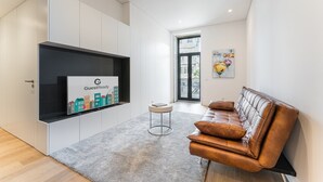 Una sala de estar moderna con un sofá de cuero marrón, un televisor de pantalla plana montado sobre un mueble blanco y una pequeña mesa redonda.